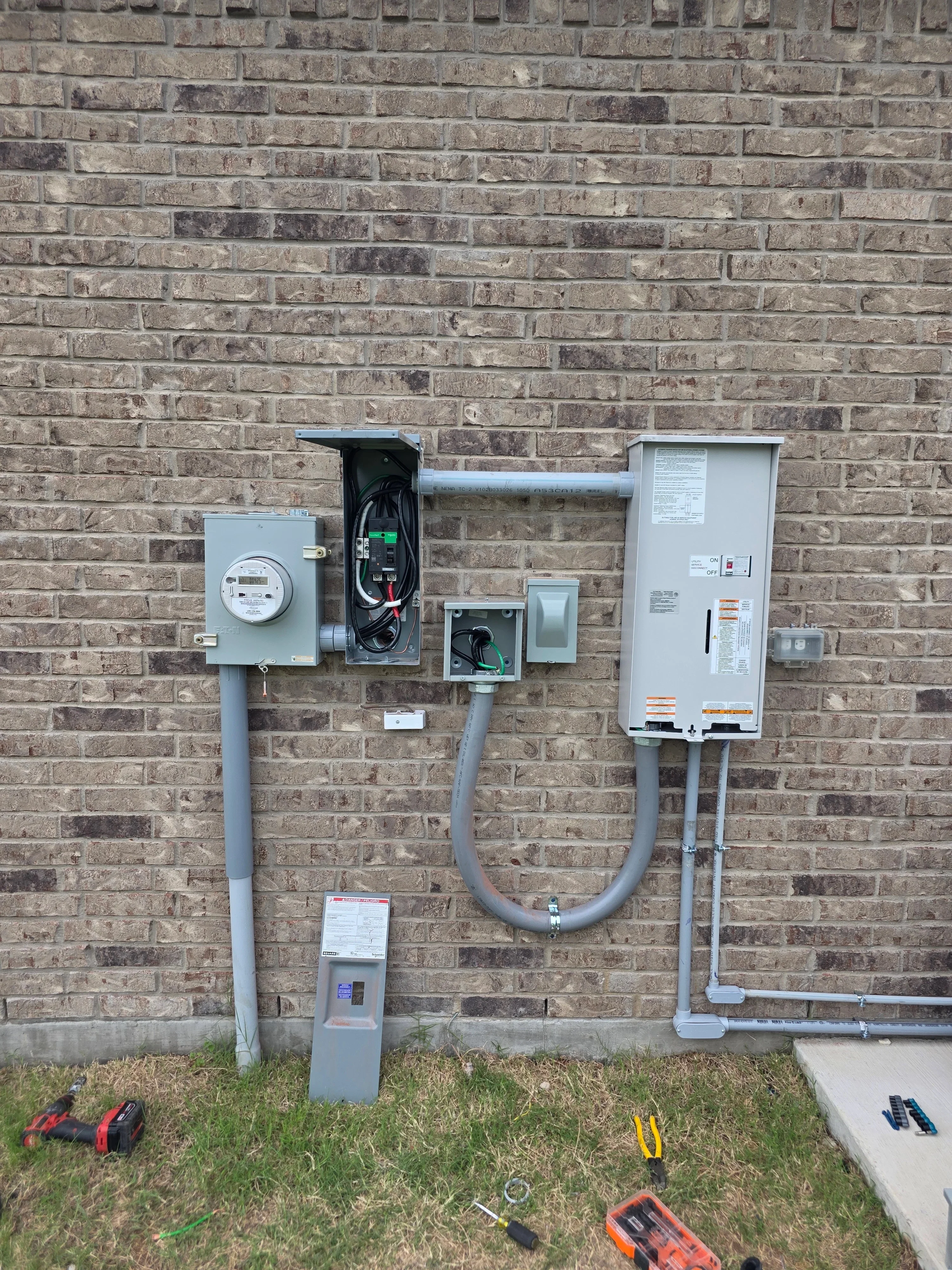 Exterior brick wall with installed electrical meter, main panel, and disconnect switch with gray conduit