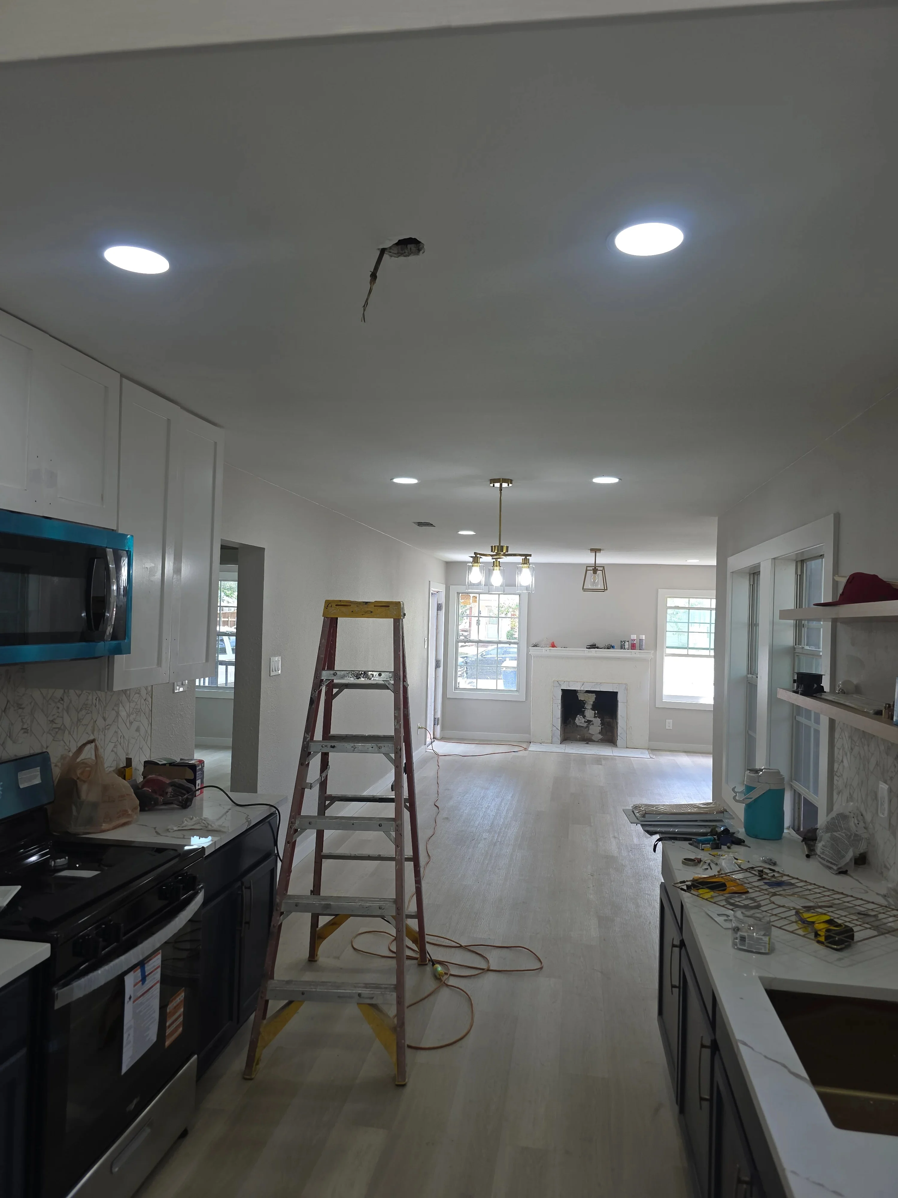 Recessed LED ceiling lights and pendant fixtures installed in kitchen-living area with white drywall