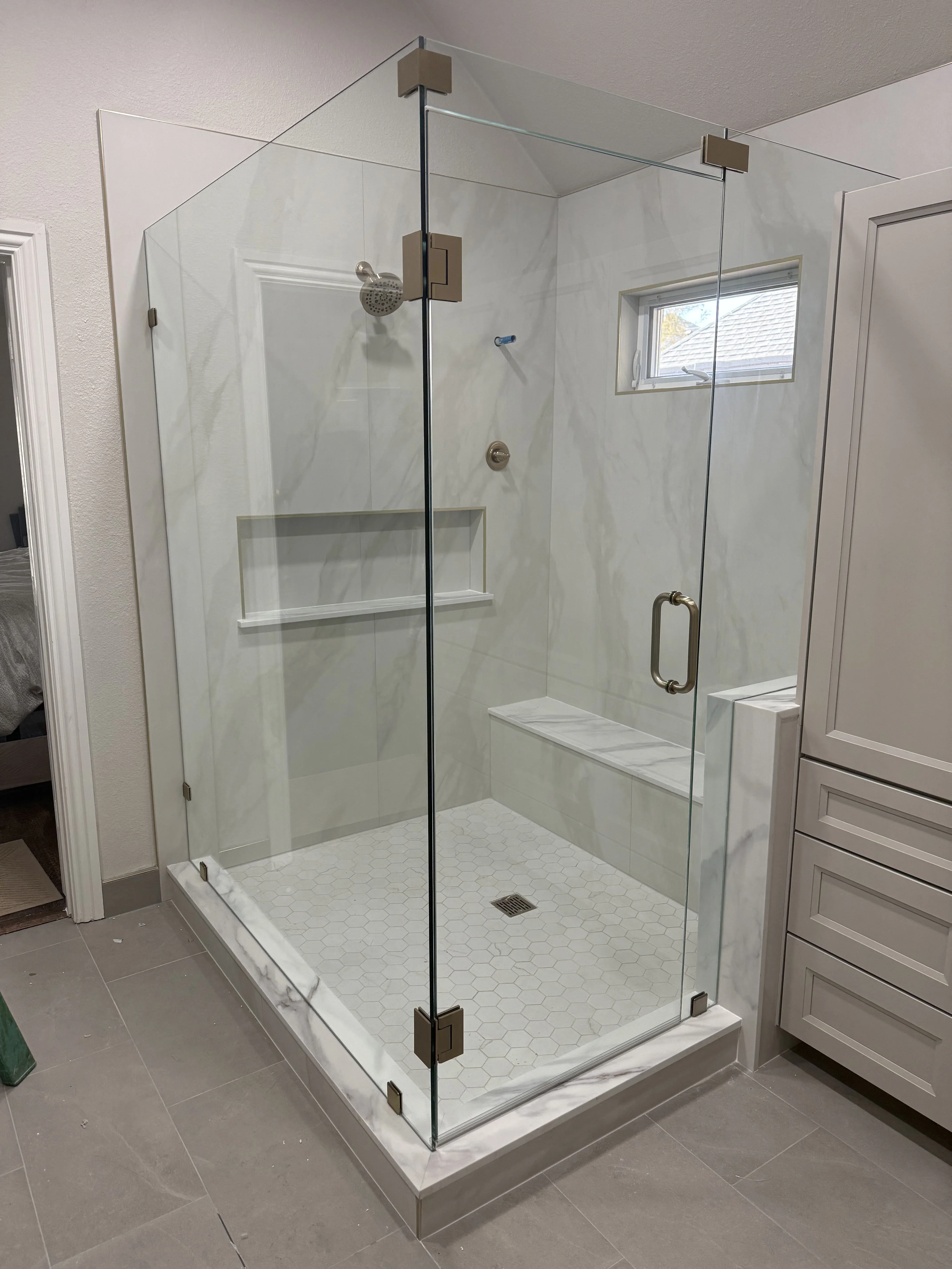 Frameless glass shower enclosure with marble hexagon tile floor and brushed nickel hardware