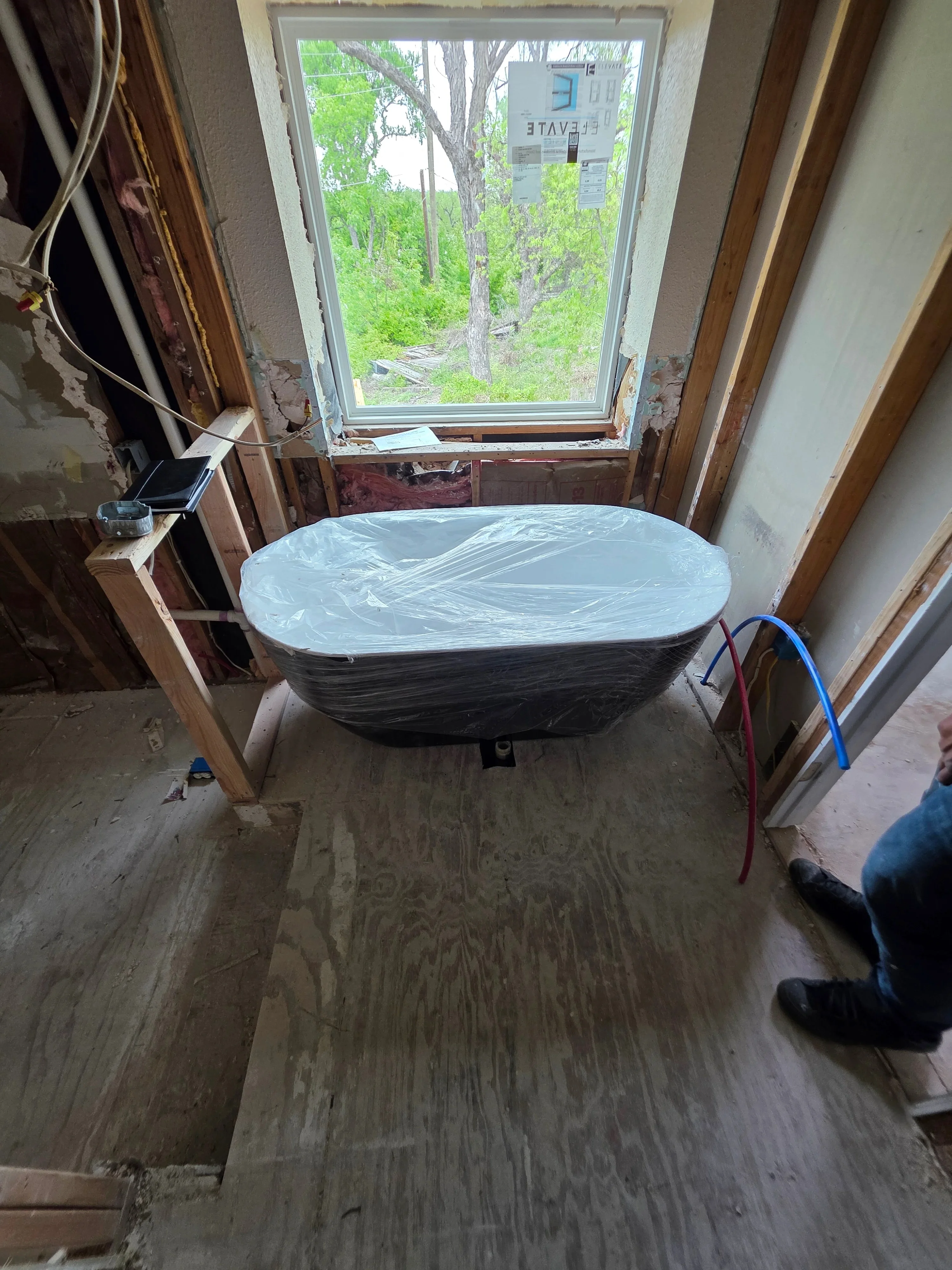 Freestanding black soaking tub with electrical rough-in wiring and blue conduit visible in bathroom under construction