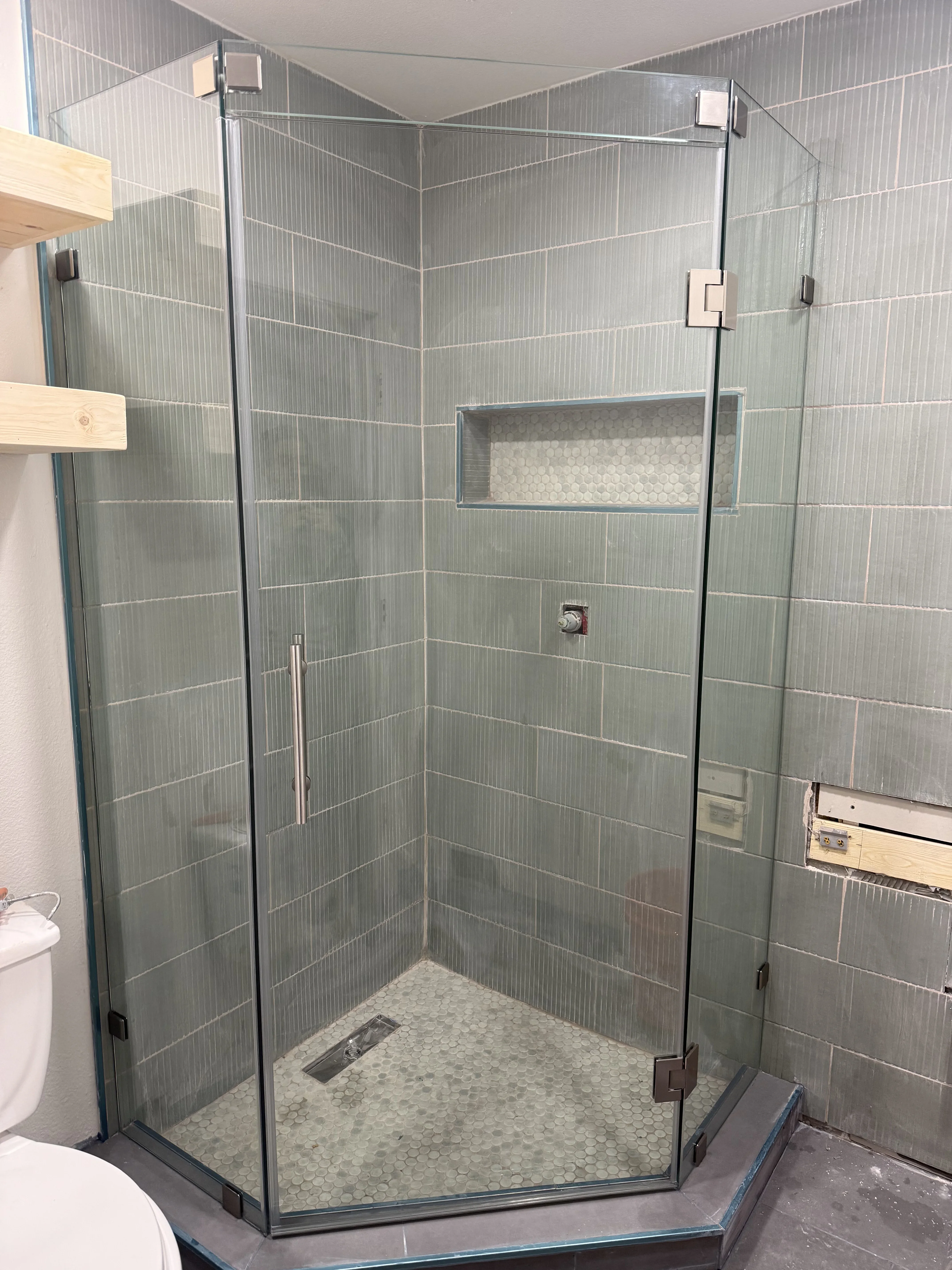 Frameless glass shower with gray subway tile walls, brushed nickel hardware, and pebble stone floor