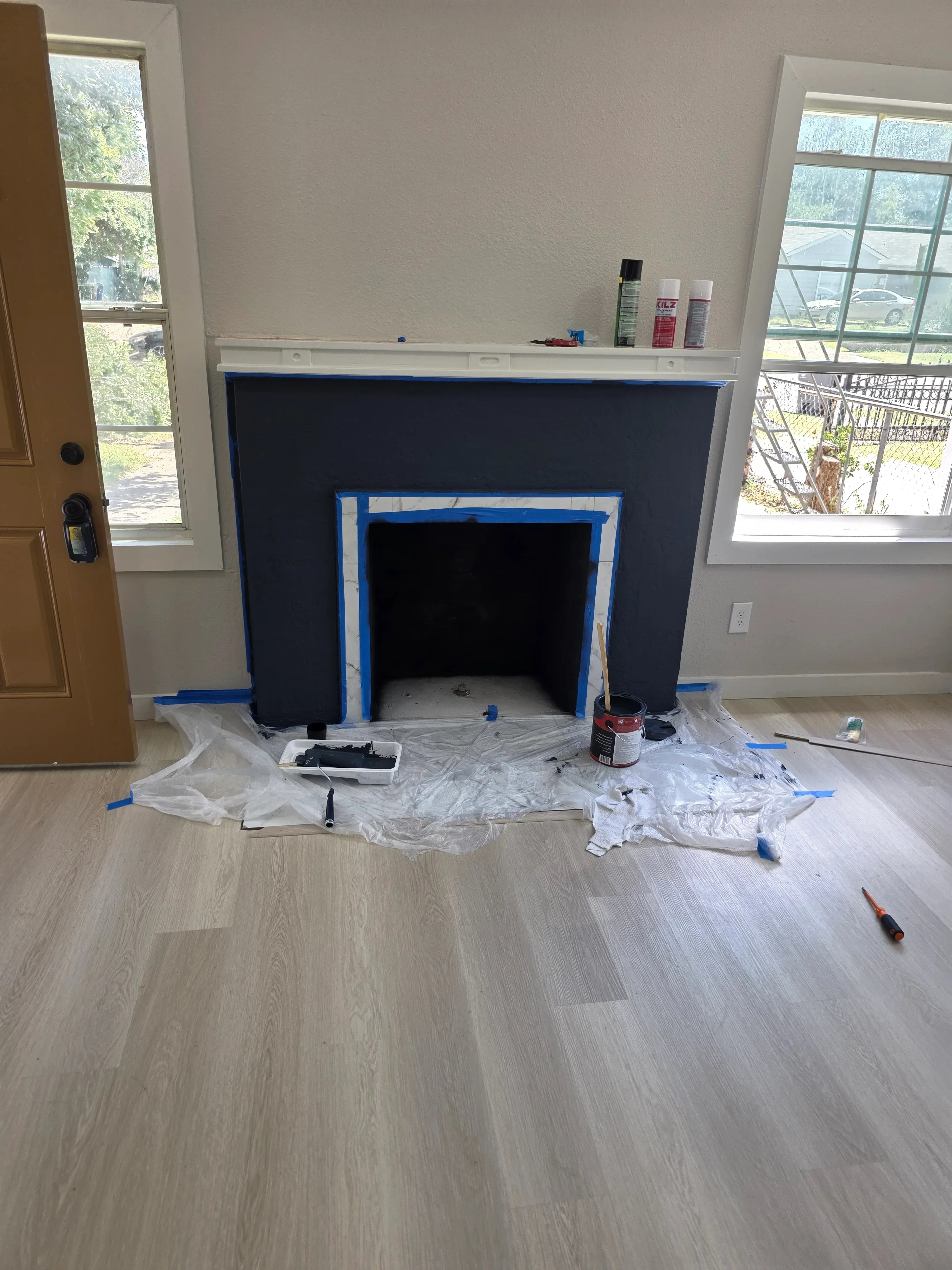 Navy blue fireplace surround with white trim, painter's tape, and drop cloth protection on hardwood floor