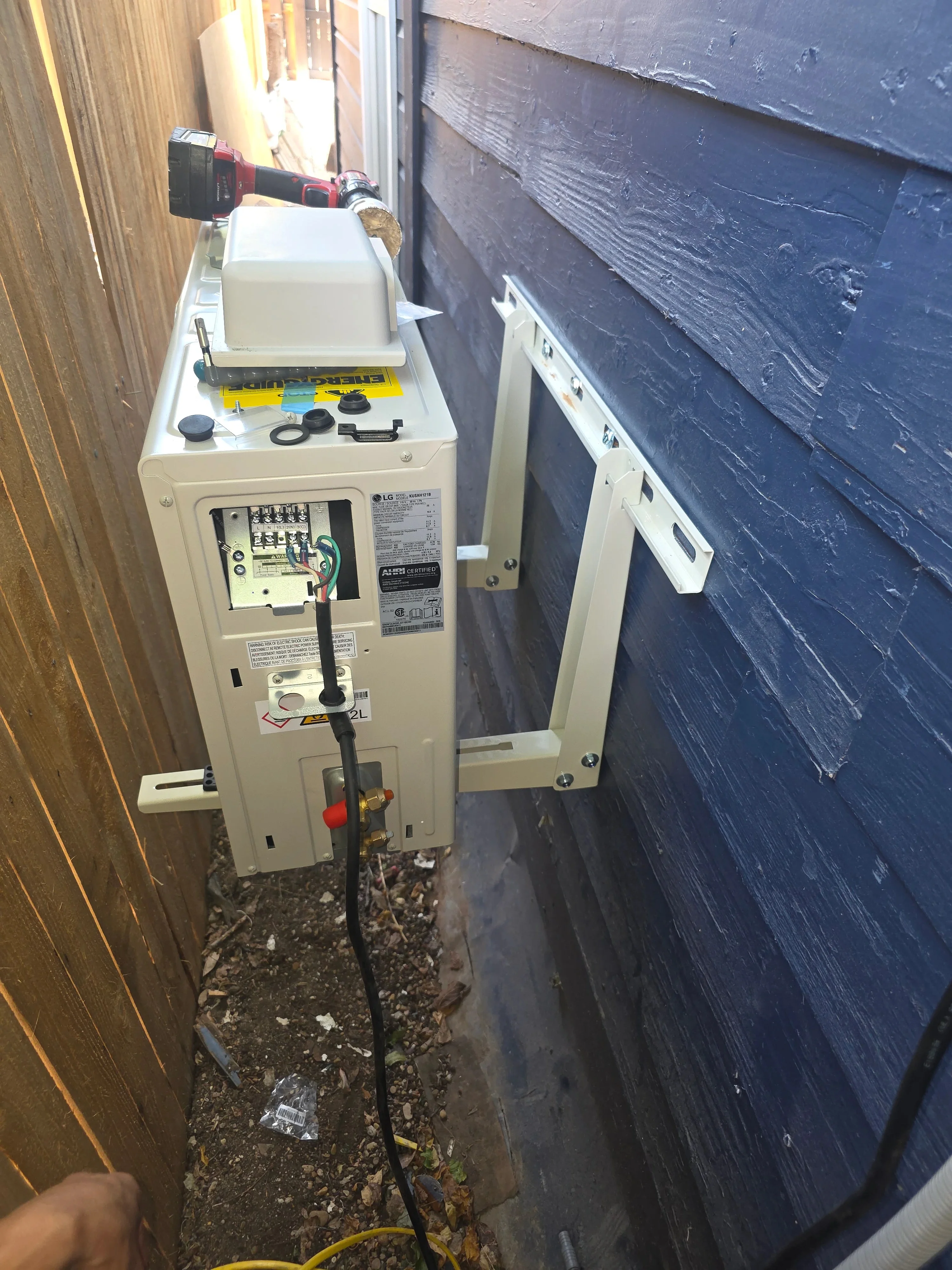 LG heat pump unit with exposed electrical panel and wiring connections in side yard installation