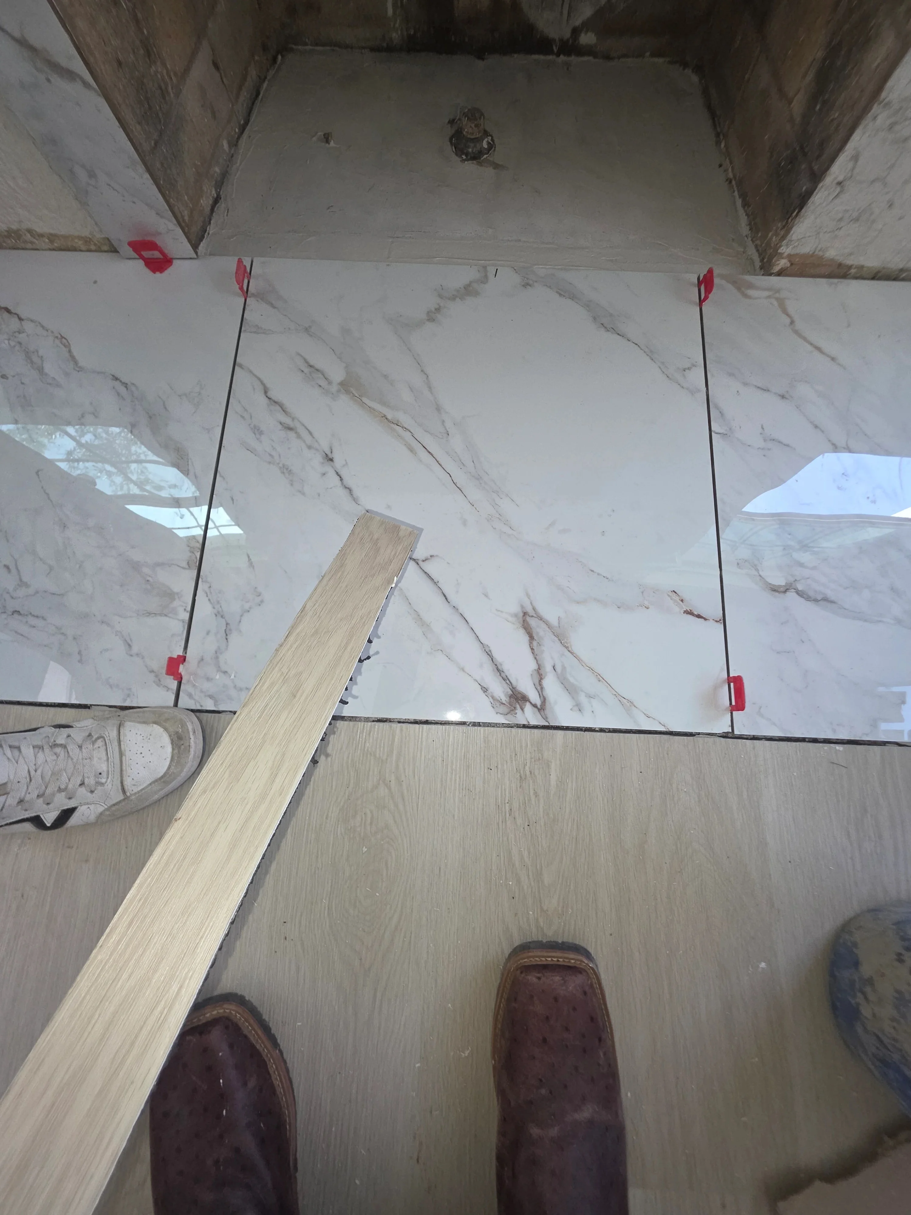 Marble tile floor installation with spacers and wooden transition trim in progress