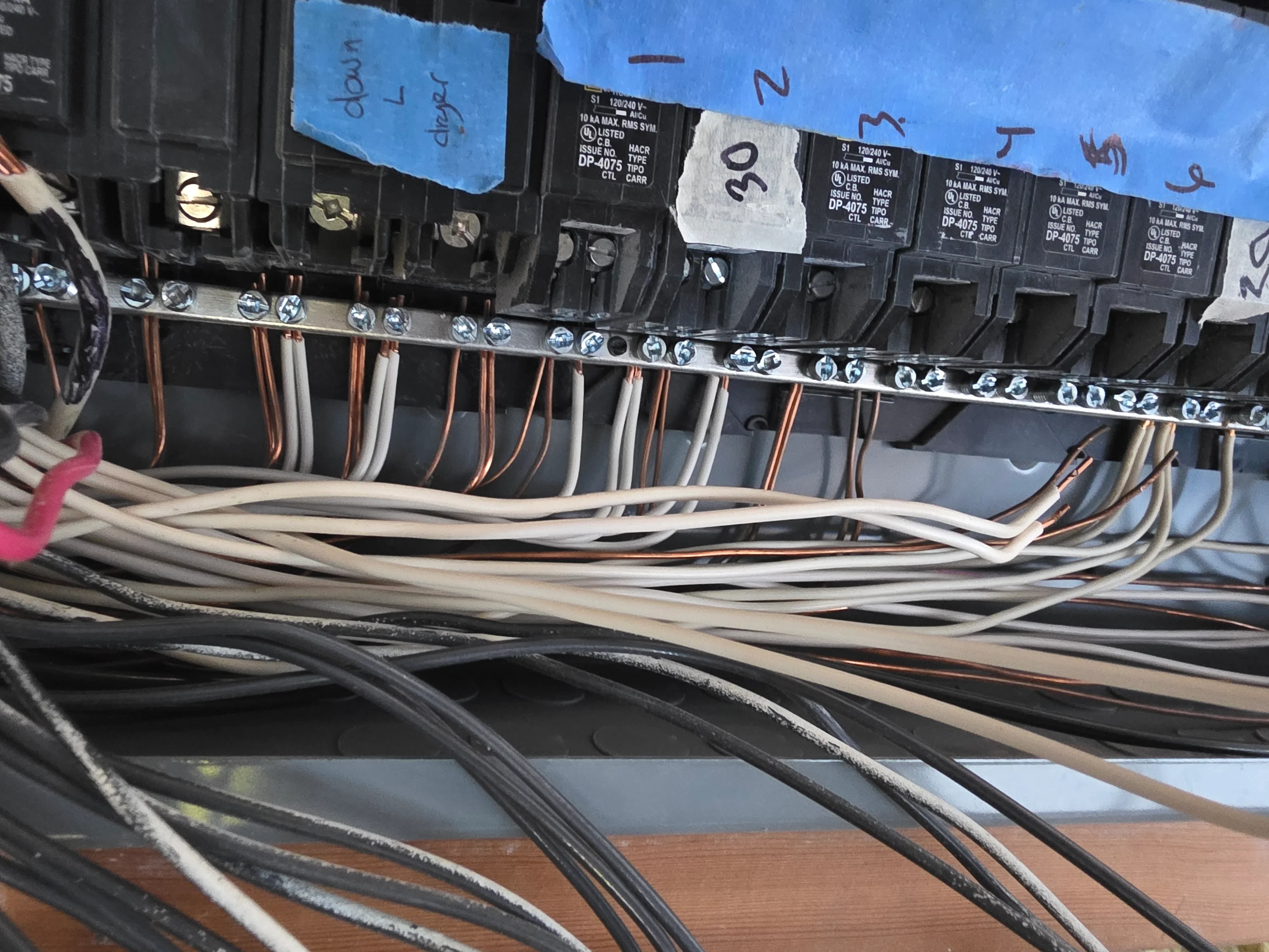 Electrical panel with circuit breakers, copper and white wiring, labeled terminals, and organized wire routing