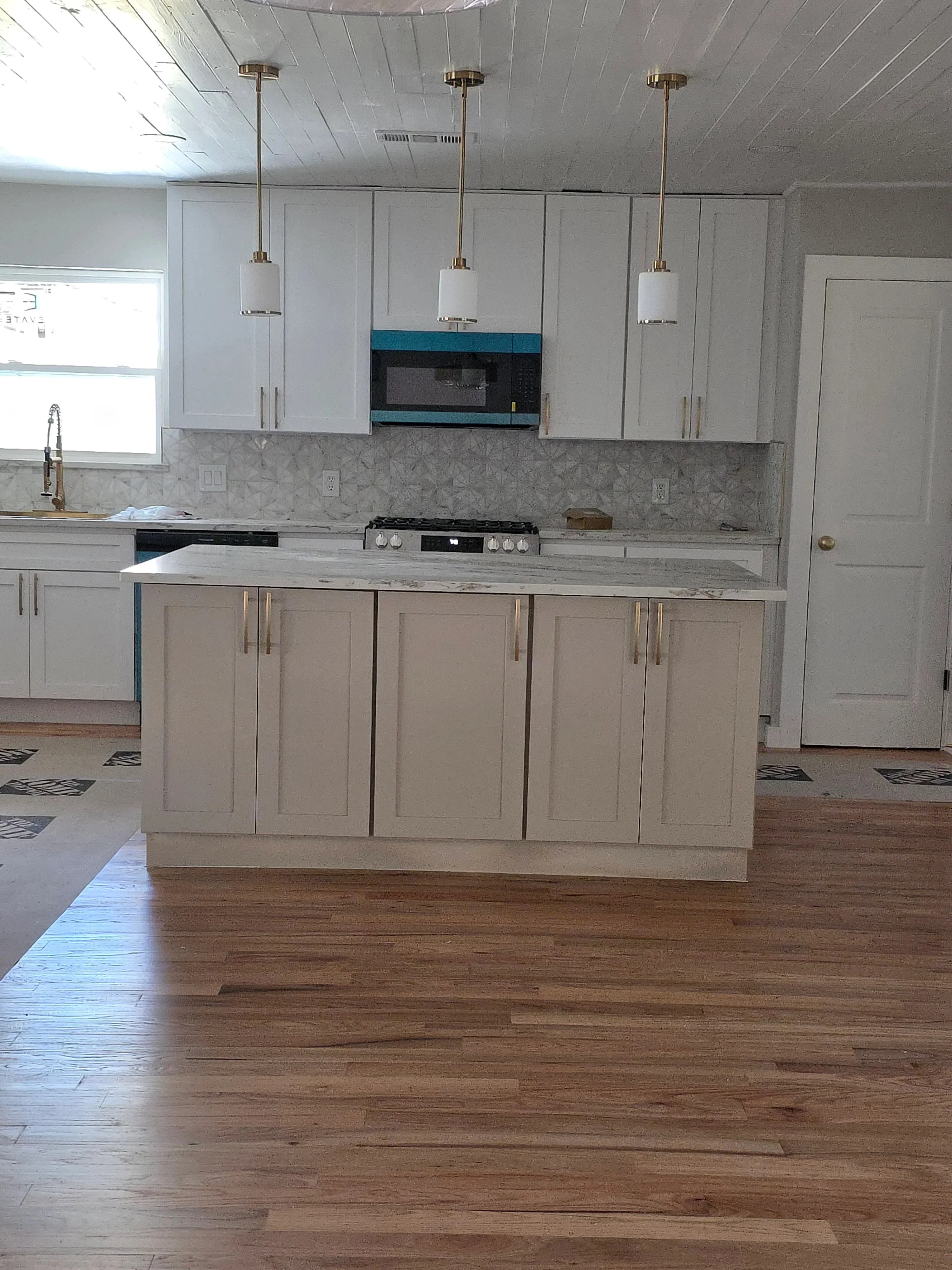 Three brass pendant lights with frosted glass shades over kitchen island with white cabinetry and marble backsplash
