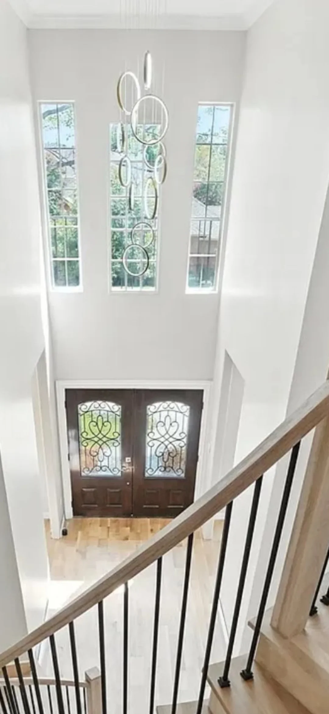 Multi-tier circular pendant light fixture installed in white foyer above decorative double doors