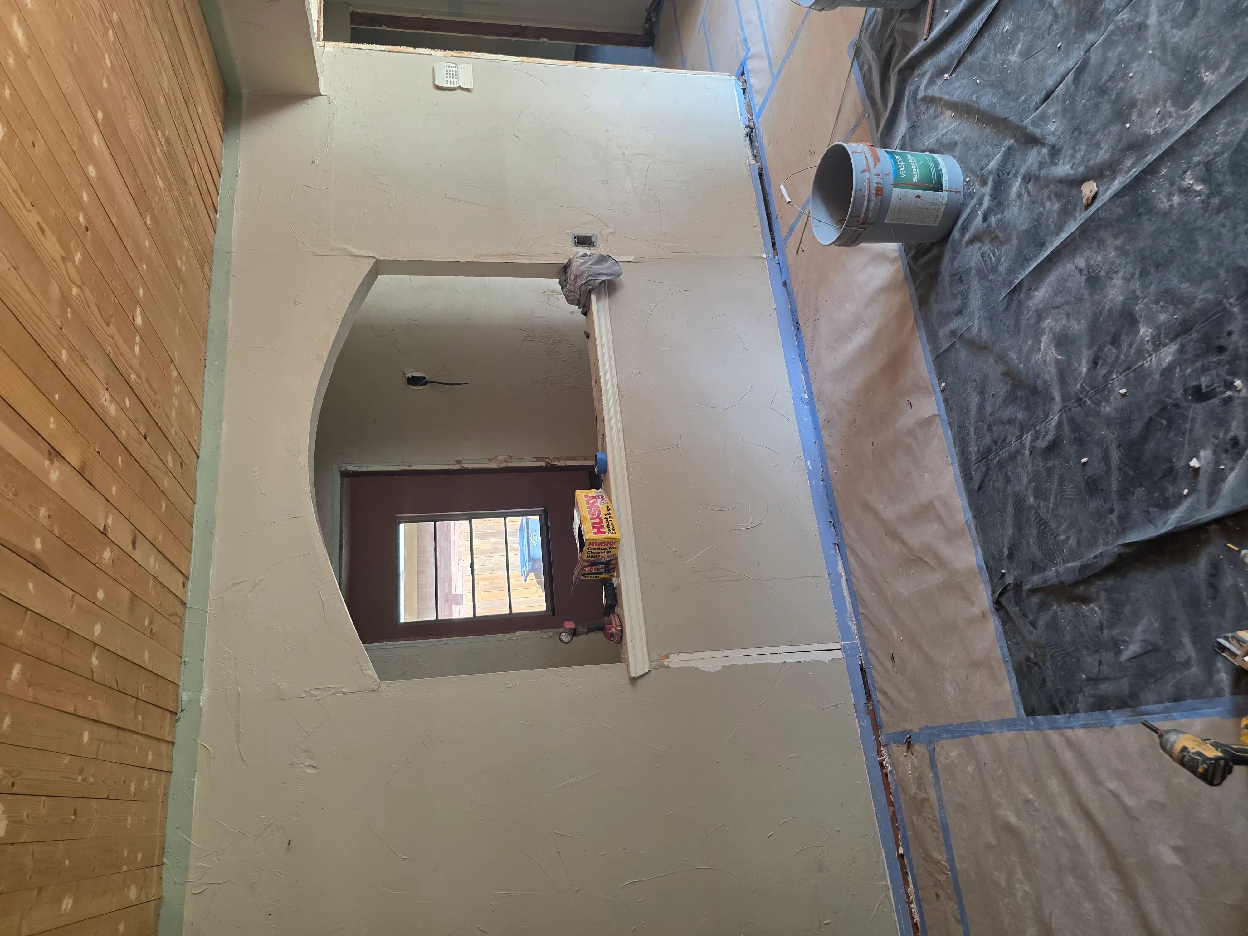 Drywall interior with electrical boxes, blue protective sheeting, and paint can on floor