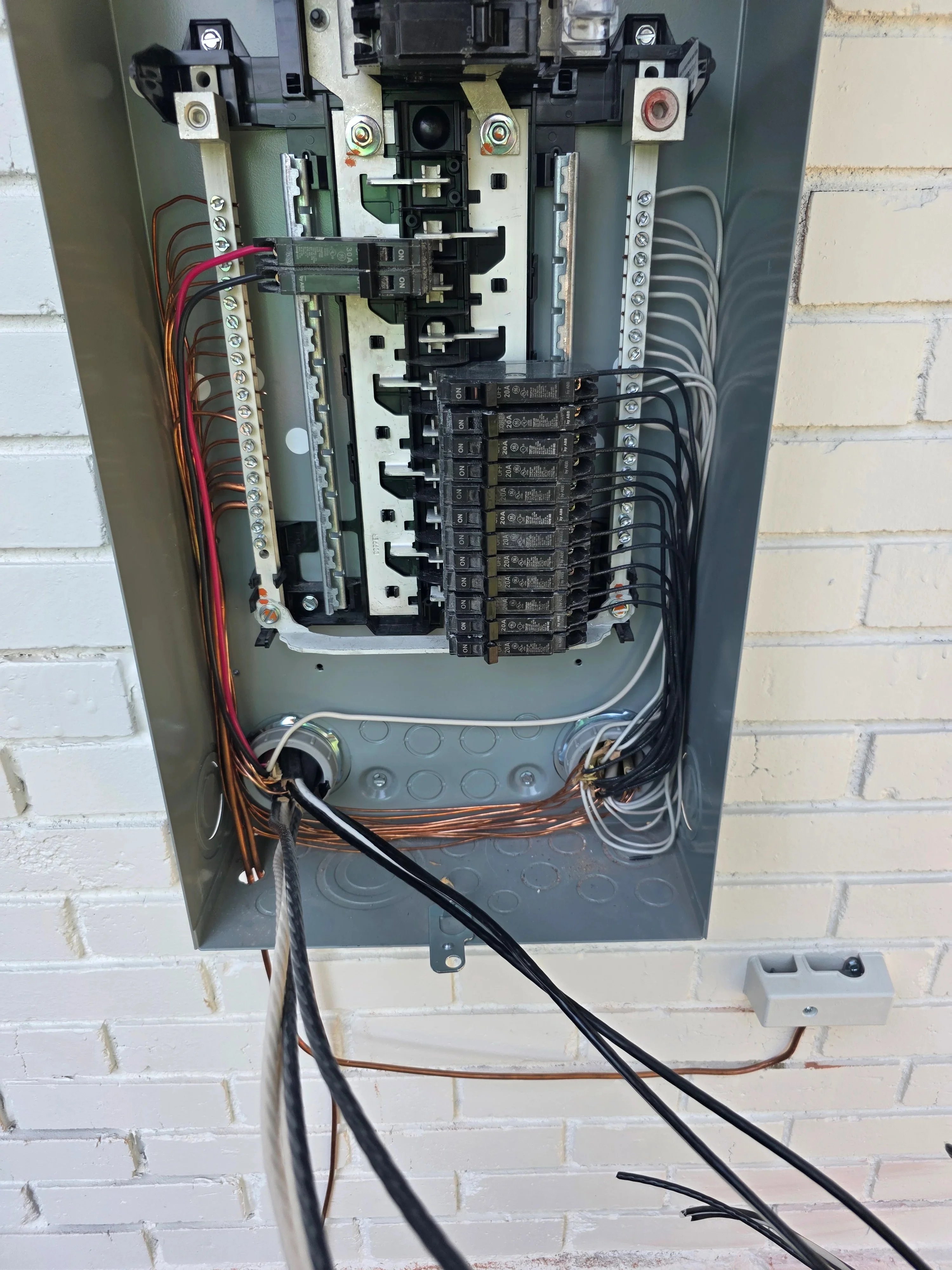 Electrical panel with breakers, organized wiring, and color-coded conductors on brick wall