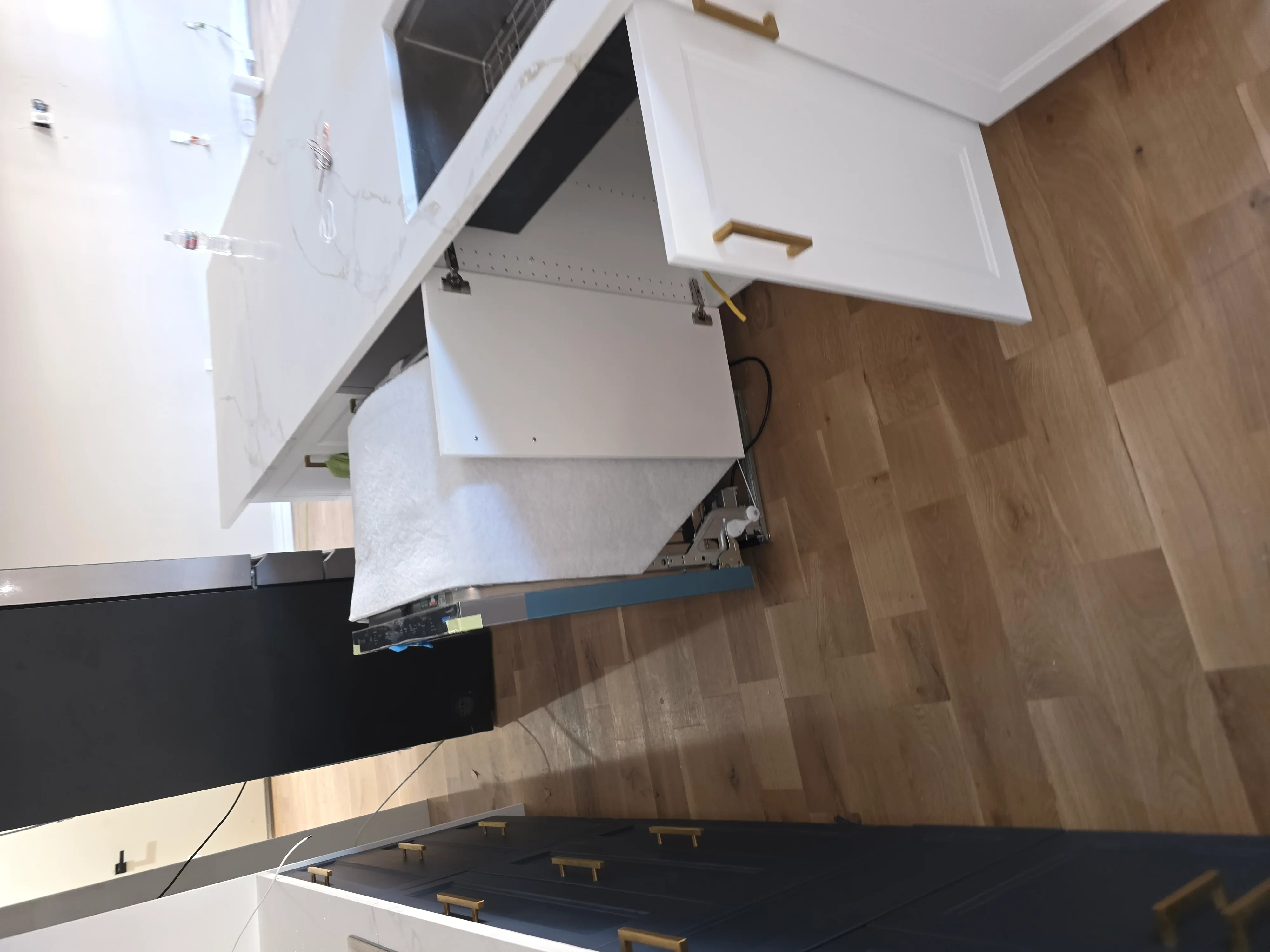 White kitchen cabinets with brass handles, electrical wiring, and wood flooring installation