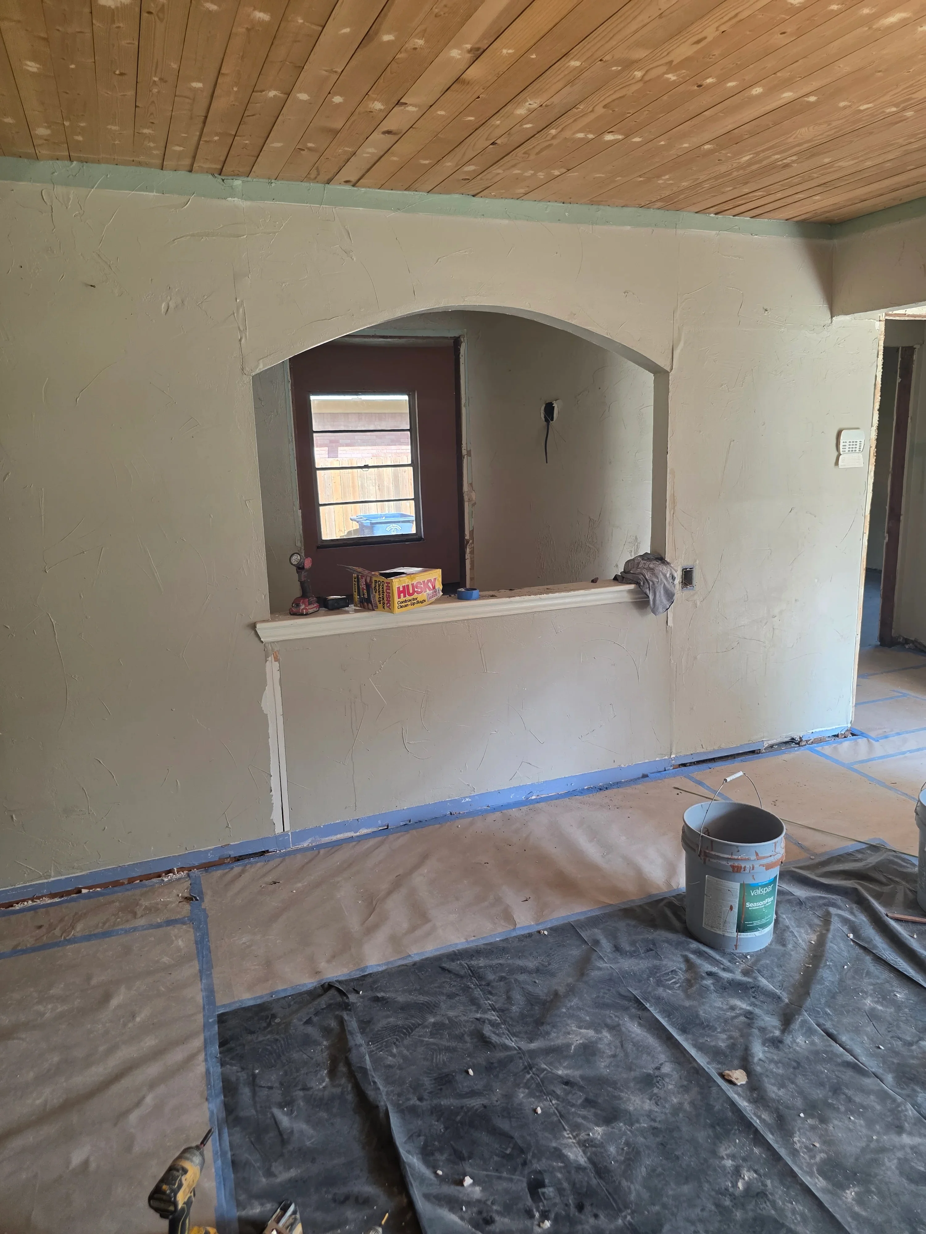 Drywall walls with archway opening, electrical outlet box, wood ceiling, and construction protection