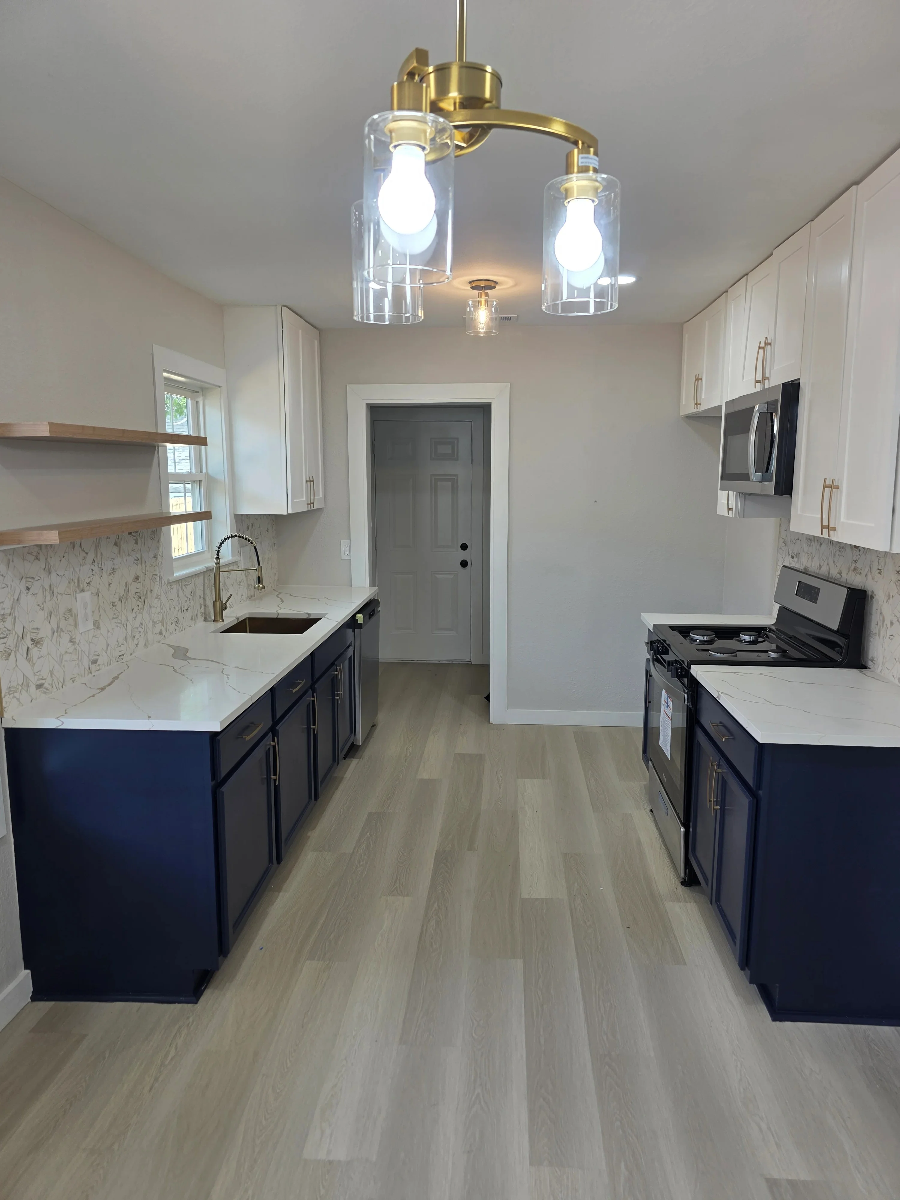 Brass dual-pendant light fixture with clear glass shades over white and navy kitchen island