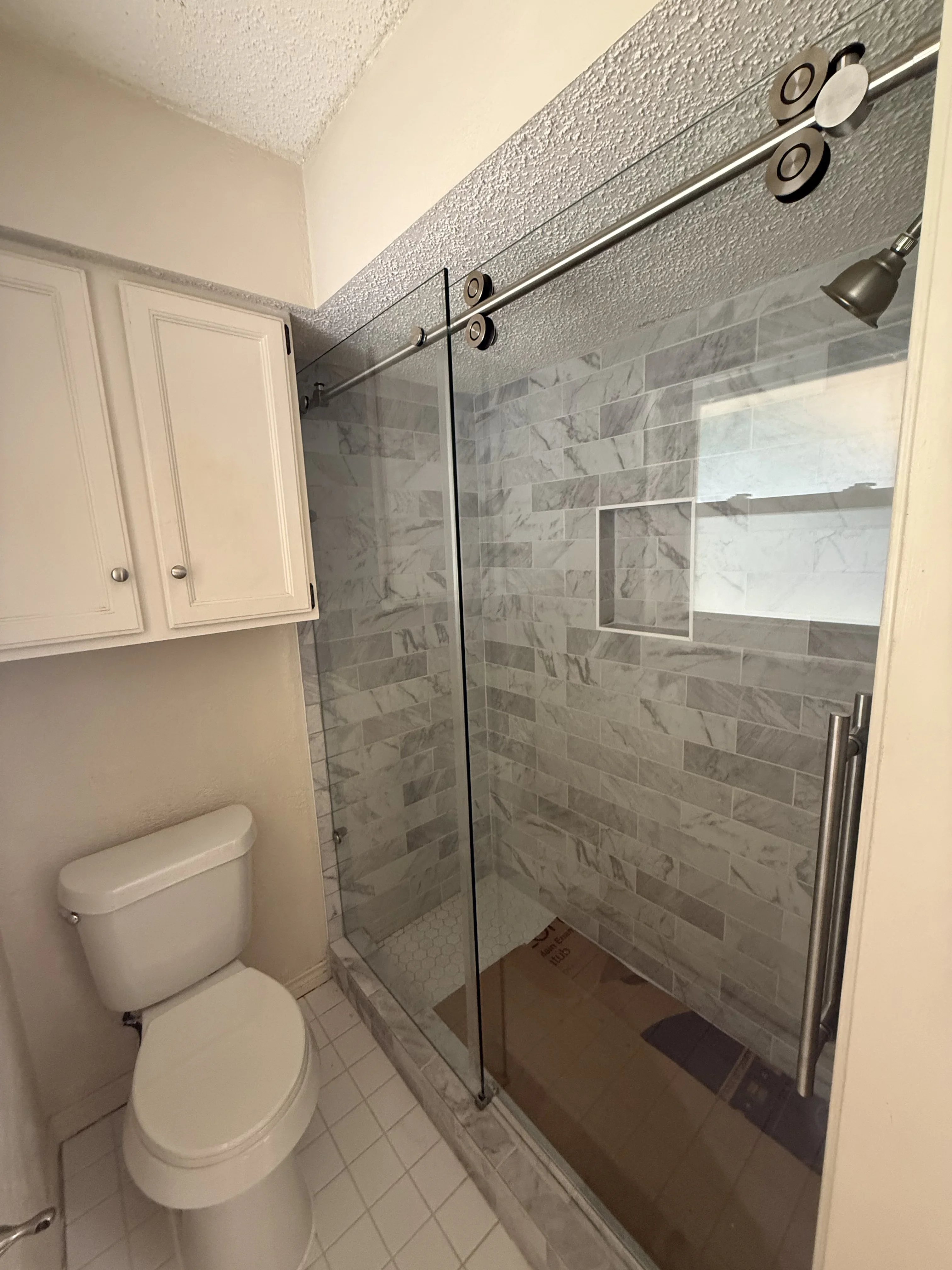 Frameless glass shower enclosure with gray marble subway tile, brushed nickel fixtures, and sliding glass doors