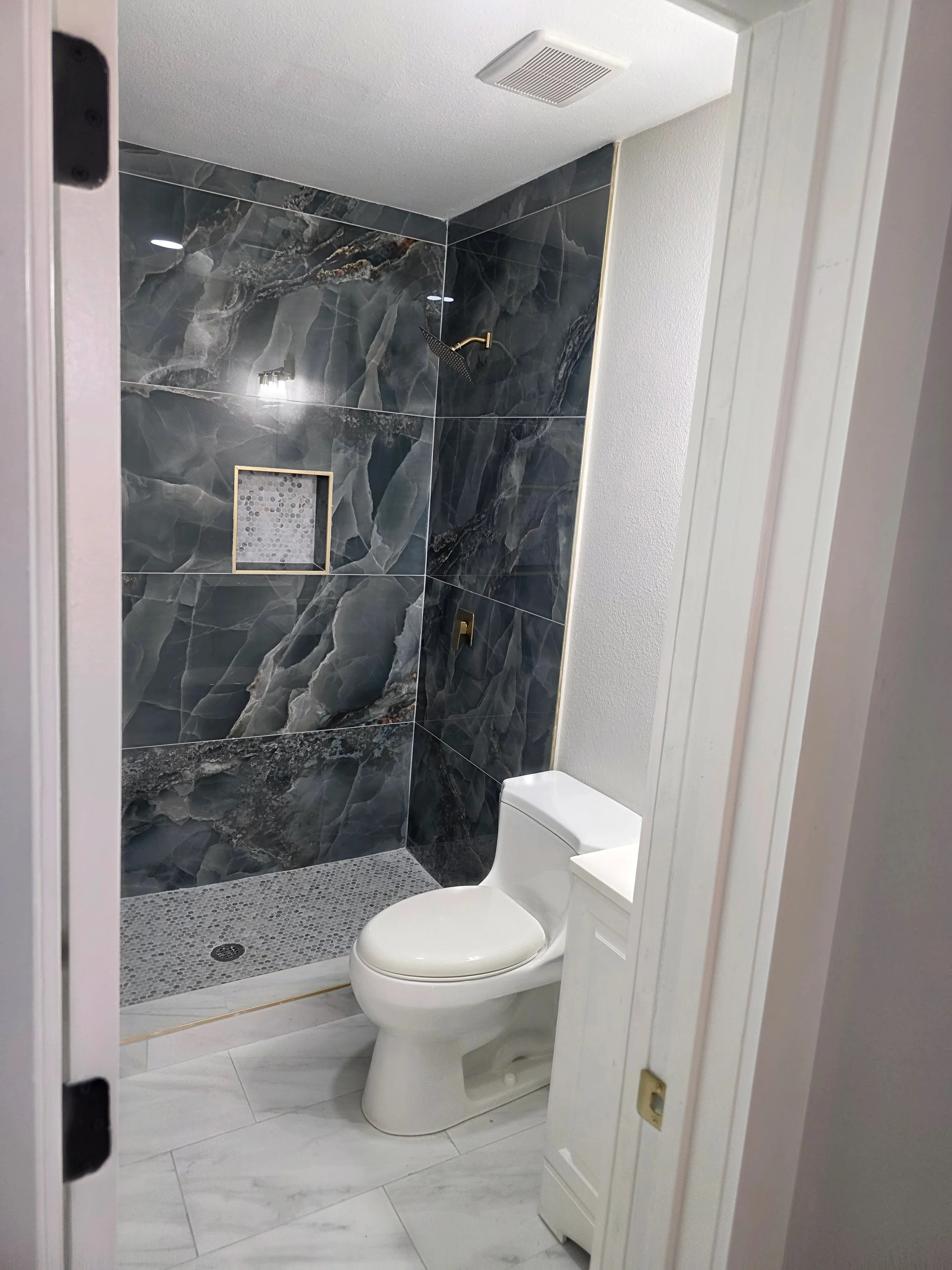 Bathroom with recessed ceiling light, exhaust fan, and shower lighting in marble tile enclosure