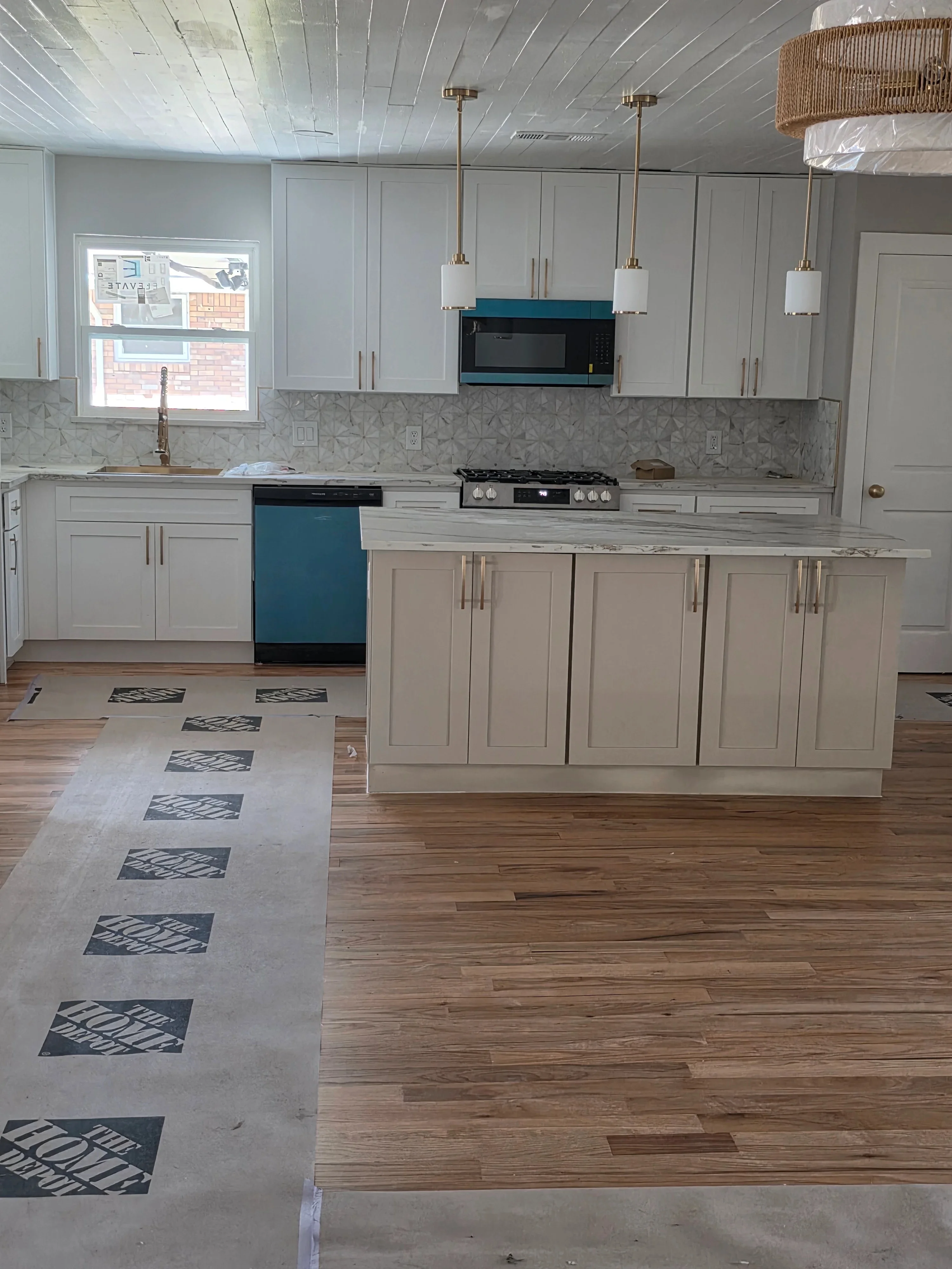 Kitchen with three brass pendant lights over island, white cabinets, geometric backsplash, hardwood floors