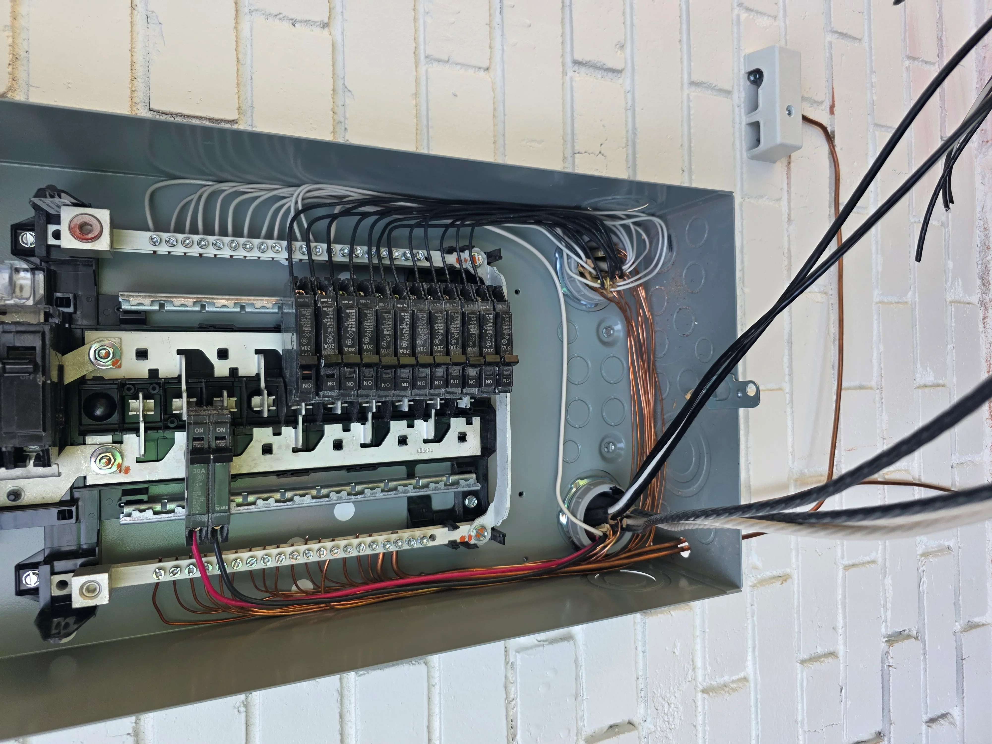 Electrical panel with breakers, copper wiring, and organized circuit connections on white brick wall