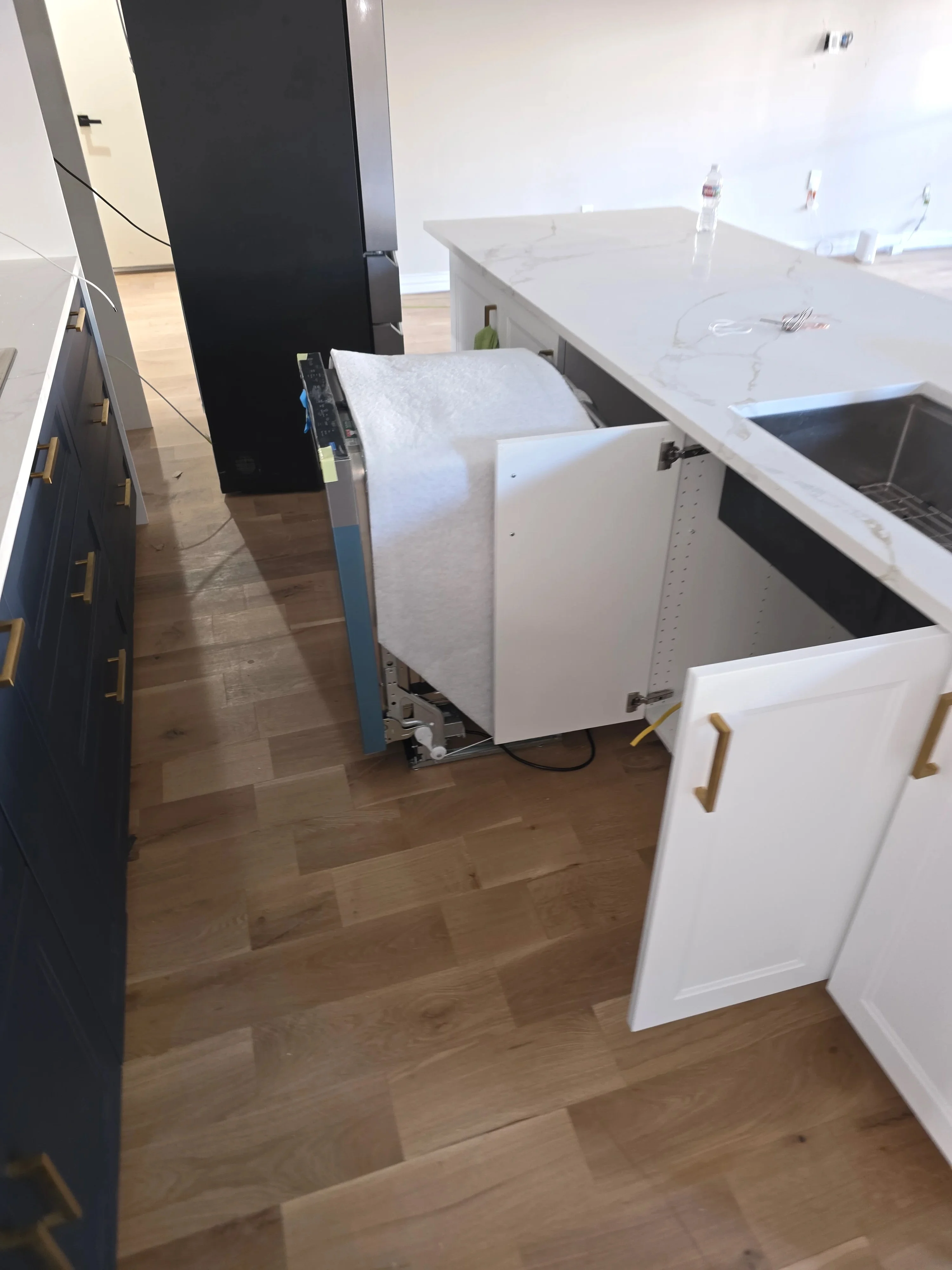 White kitchen cabinets, quartz countertops, stainless steel sink, and hardwood flooring during installation