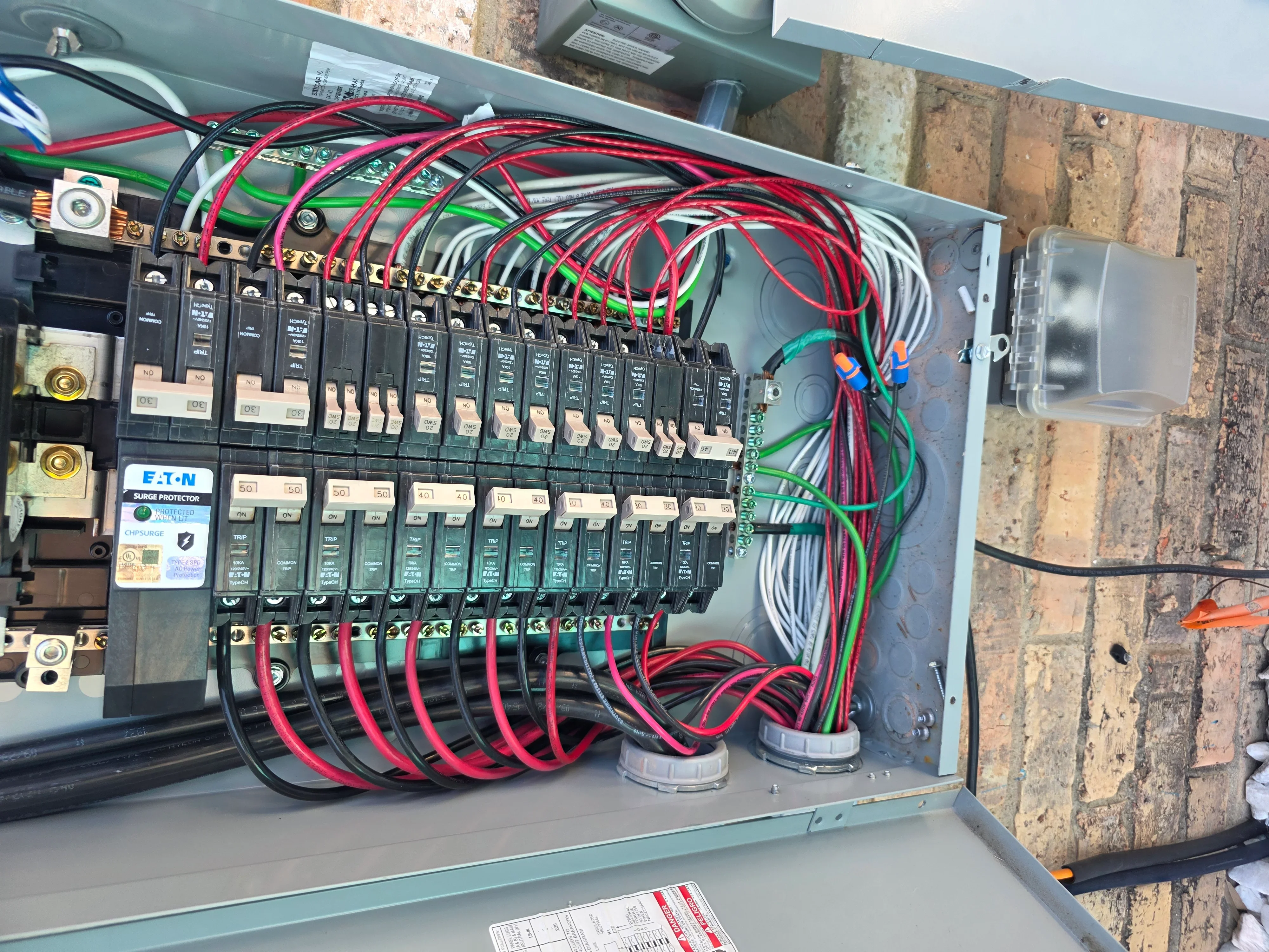 Electrical panel with multiple breakers, red and green circuit wires, and brass connectors installed in metal enclosure